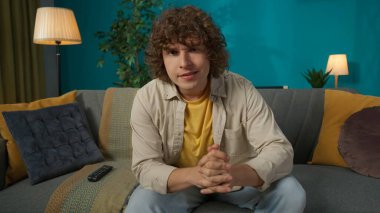 Oturma odasındaki kanepede günlük giysiler içinde oturan genç bir erkek modelin yakın plan fotoğrafı. TV 'de sırayla haber izliyor..