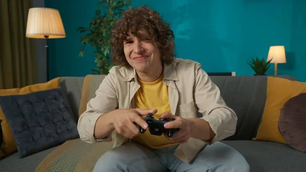 一个年轻男子坐在客厅沙发上的画像 男人玩一个游戏机 他因为输了一场比赛而很难过 — 图库照片