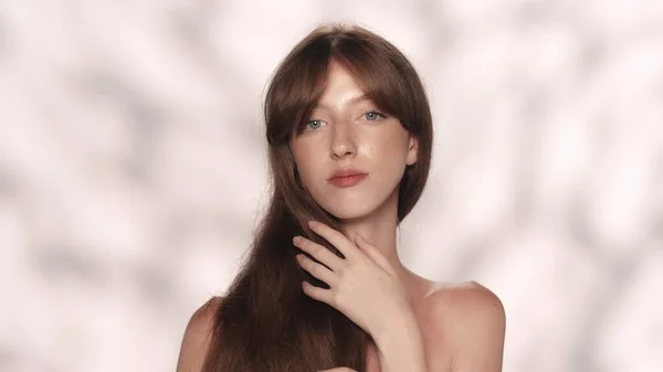 美しいブルネットの肖像画 カメラを見ている彼女の光沢のある髪に触れる青い目を持つ少女モデルの近くのショット ビューティーケア広告コンセプト — ストック写真