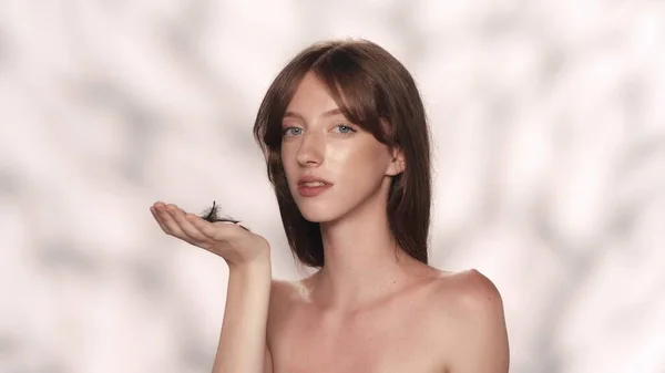 美しい白人モデルの肖像画 彼女の手に小さな羽を持ってカメラを直接見ている女性のショットを閉じます スキンケア広告コンセプト — ストック写真