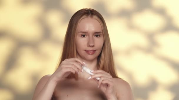 若い女性はしわを防ぐために目の周りの皮のために持ち上がるローラーのゲルを使用します ハイライト付きの黄色の背景にあるスタジオのセミノードの女性 ケアのコンセプト — ストック動画