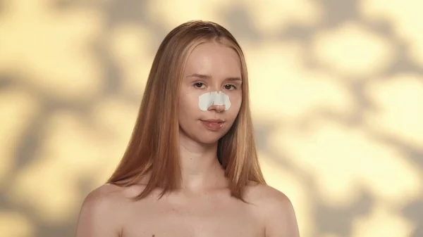 妇女执行化妆品面部皮肤护理程序 一个鼻梁上有黑头斑斑的女人的画像 工作室里的一个聪明女人 背景是黄色的 有亮点 — 图库照片