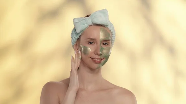 女人在脸上涂上绿色的化妆品面具 光彩夺目的女人在工作室的头发带黄色背景与亮点 护肤和治疗 — 图库照片