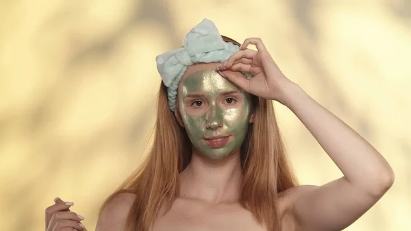 一个女人从绿色的清洁面罩上剥下 光彩夺目的女人 脸上带着绿色的面具 背景是黄色的 背景上有亮点 抗衰老 起皱面膜 — 图库照片
