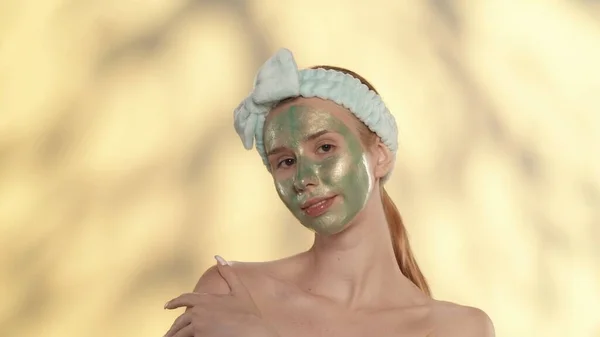 頭にヘアバンドを持つ若い女性は 美容スキンケアの手順を実行します ハイライト付きの黄色の背景のスタジオで彼女の顔に緑のマスクを持つセミナーの女性の肖像画 — ストック写真