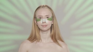Genç bir kadın gözlerinin altında yeşil hidrojel yamalar açıyor. Gözlerinin altında yamalar ve stüdyodaki siyah noktalardan kalma alçıyla yeşil arka planda röfleli bir kadın. Güzellik kavramı