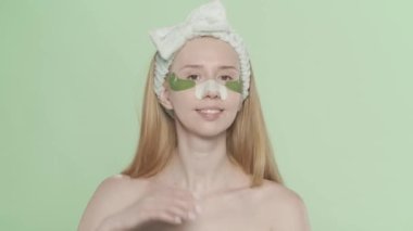 Gözlerinin altında yamalar olan yeşil bir ekranda siyah noktalar için sıva yapan bir kadın. Saç bandı olan bir kadın, estetik ameliyatlar sayesinde temiz ve pürüzsüz bir yüz ifadesi sergiliyor. Güzellik