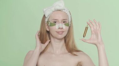 Gözlerinin altında yamalar olan bir kadın, burnunda siyah noktalardan kalma alçıyla, yeşil bir ekranda saç bandıyla. Bir kadın bir ampul saç serumu gösteriyor. Güzellik konsepti, kozmetoloji