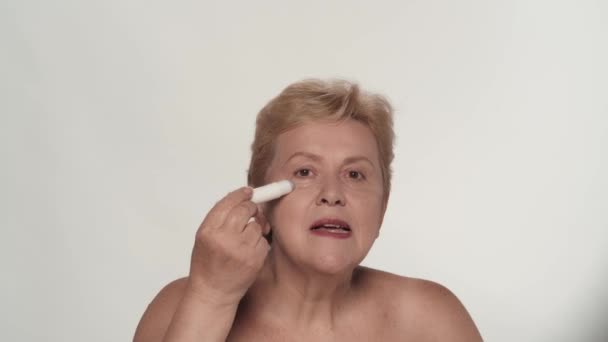 上級女性の肖像画 目の下の肌に化粧品を塗った中年の女性モデルのクローズアップショット 美容アンチエイジングスキンケア広告コンセプト — ストック動画