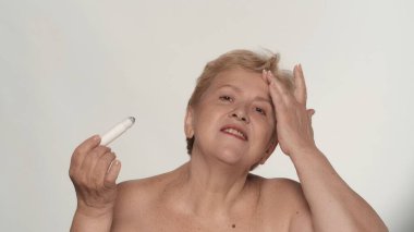 Güzel bir kadının portresi. Orta yaşlı bir kadın modelin, alnına kozmetik bir ürün sürerken, kameraya gülümserken yakın plan çekimleri. Güzellik derisi reklam konsepti.