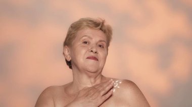 Güzel, sarışın, son sınıf öğrencisi bir kadının portresi. Orta yaşlı bir kadın modelin güneş kremi sürerken, kameraya bakarken yakın plan çekimi. Cilt koruma kavramı.