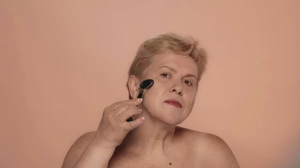一个年长女人的画像 一个中年金发女模的近照 她用滚筒进行面部按摩 并看着相机 美容美发广告理念 — 图库照片