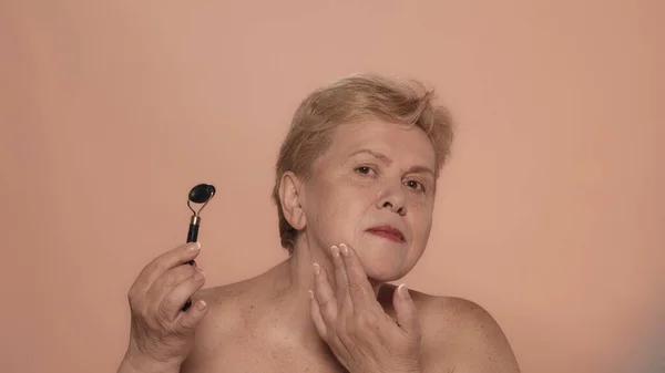 一个年长女人的画像 一个中年妇女模特儿用胶辊按摩并看着相机的近照 美容美发广告 — 图库照片