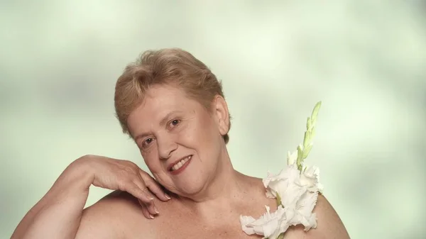 ブロンドの女性の肖像画 白いグラディオラスの花を持った中年の女性モデルのクローズアップショット カメラを見て笑顔 ビューティー広告コンセプト — ストック写真