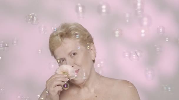 美しいブロンドの女性の肖像画 バラの花を抱えた中年の女性モデルのクローズアップショットと カメラで笑顔で たくさんの石鹸の泡が飛び回っています スローモーションHdr — ストック動画