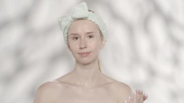 Bir kadın yüzüne yeşil bir kozmetik maske takıyor. Stüdyoda saç bandı takmış gri arka planda parlak saçlı bir kadın. Güzellik derisi ve tedavi HDR BT2020 HLG Malzemeleri.