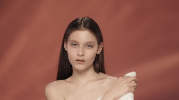 若い女性が白いテリータオルで顔と裸の肩を拭く 赤い背景のスタジオにいる女性 スキンケアのコンセプト — ストック動画