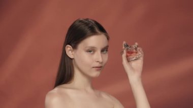 Bir kadın şişeden parfüm sıkar, aromayı sever. Stüdyoda kırmızı arka planda bir şişe parfümlü bir kadın. Parfüm ve aroma terapisi. Güzellik, kozmetoloji, özen kavramı