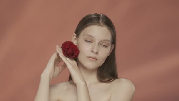 女性は顔の近くに赤いバラの芽を抱え 手の柔らかく滑らかな肌に触れます レッドバックのスタジオでセミナーの女性の肖像画 化粧品 ケアHdrのコンセプト — ストック動画