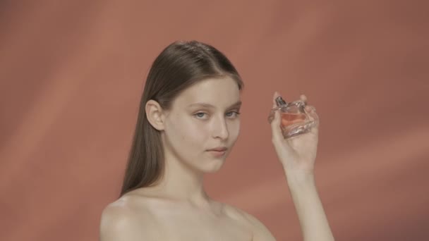 女性は瓶から香水をスプレーし 香りを楽しむ 赤い背景のスタジオで香水の瓶を持ったセミノードの女性 香水とアロマセラピー ケアのコンセプト — ストック動画