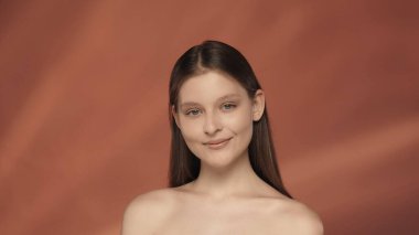 Stüdyoda kırmızı arka planda gülümseyen genç bir papaz yardımcısının portresi. Doğal güzellik kavramı, kozmetoloji, cilt bakımı.