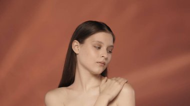 Genç bir kadın, pürüzsüz, ipeksi tenine dokunarak zevk alır. Stüdyoda kırmızı arka planda duran bir kadının portresi. Güzellik konsepti, kozmetoloji, cilt bakımı