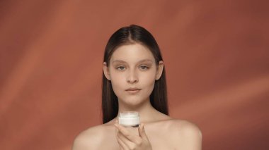 Bir kadın bir kavanoz kozmetik kremi tutuyor. Stüdyoda kırmızı arka planda bir kavanoz kremalı bir kadın. Güzellik, kozmetoloji, özen kavramı