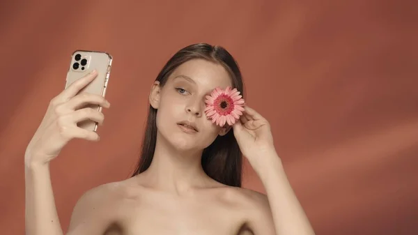 一个女人拍了一个视频 拿了一个自拍 一只眼睛盖满了粉红的芙蓉花 带着红色背景的女人站在演播室里 美容美发 美容美发 治疗和护理的概念 — 图库照片