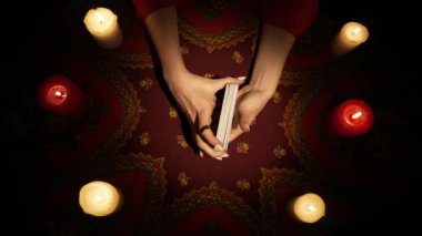 Falcı seansı sahnesi, üst manzara. Masadaki mumlarla çevrili tarot kartlarını karıştıran kadın ellerini yakın plan çekimde çek. Kadın kehanete hazırlanıyor. Esrarengiz kavram.