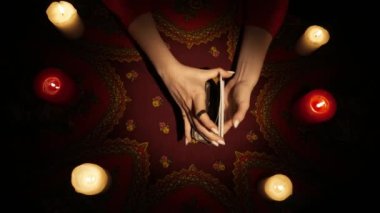 Falcı seansı sahnesi, üst manzara. Tarot kartlarını karıştıran, güverteden birkaç kart seçen ve kartları masaya koyan bir kadının yakın çekim görüntüsü. Esrarengiz kavram.