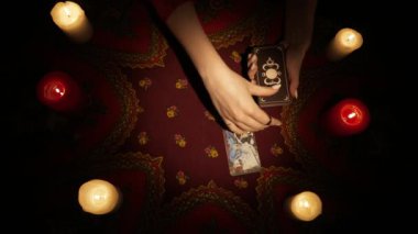 Falcı seansı sahnesi, üst manzara. Bir bayanın el ele tutuşup, elinde bir sürü kart tutarken ve masanın üzerinde bir hayran tarot düzeni oluştururken yakın plan çekimleri. Öngörü kavramı.