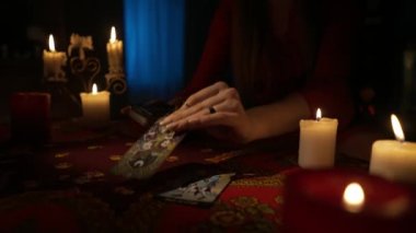 Odada, masada oturan kadının, etrafında bir sürü mumla yakın çekimini yap. Kadın model, güverteden tarot kartlarını alıyor, bir plan yapıyor. Kişisel kehanet kavramı.
