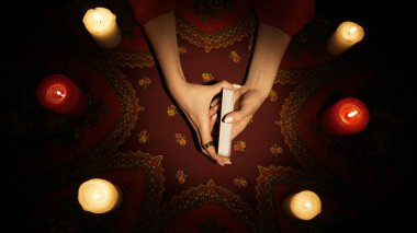 Falcı seansı sahnesi. Masanın üzerinde mumlarla çevrili tarot kartlarını tutan kadınların yakın çekimleri. Kadın kehanete hazırlanıyor..