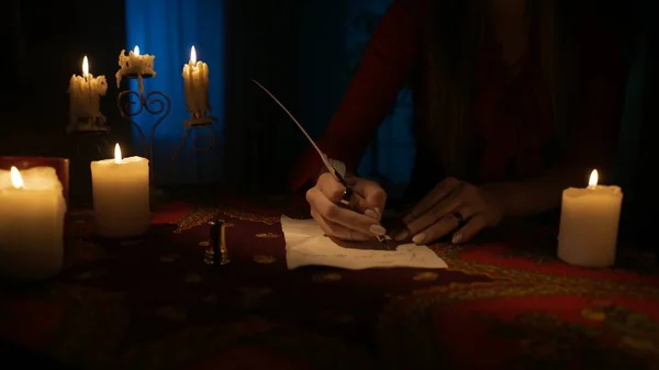 一个女人坐在桌子上 身边拿着许多蜡烛 她用毛笔在旧纸上写了些什么 神奇的美学概念 — 图库照片