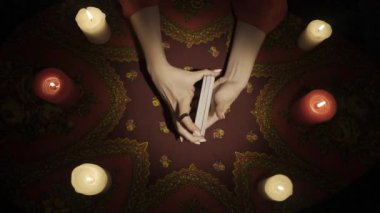 Falcı seansı sahnesi, üst manzara. Masadaki mumlarla çevrili tarot kartlarını karıştıran kadın ellerini yakın plan çekimde çek. Kadın kehanete hazırlanıyor. Esrarengiz bir kavram. HDR BT2020 HLG