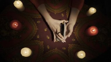 Falcı seansı sahnesi, üst manzara. Tarot kartlarını karıştıran, güverteden birkaç kart seçen ve kartları masaya koyan bir kadının yakın çekim görüntüsü. Esrarengiz bir kavram. HDR BT2020 HLG Malzemesi.