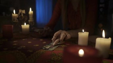 Odadaki masanın etrafındaki mumlarla yakın plan çekimini yap. Kadın model, masadaki güverteden bir sürü tarot kartı çıkarıyor. Kişisel kehanet konsepti. HDR BT2020 HLG Malzemesi.