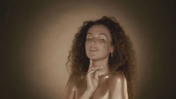 側面を見ている若い魅力的な女性のショットを閉じ 金メイク アクセサリーで彼女の顔に触れる ゴールデン ドリップ ブラウンの背景 美と化粧品の広告 — ストック写真