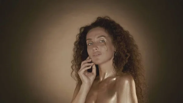 側面を見ている若い魅力的な女性のショットを閉じ 金メイク アクセサリーで彼女の顔に触れる ゴールデン ドリップ ブラウンの背景 美と化粧品の広告 — ストック写真