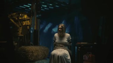 Korku filmi sahnesi. Beyaz elbiseli manyağın sarışın kadın kurbanı depoda sandalyede oturuyor. O bir iple bağlandı. Hokey maskeli bir adam onun önünde elektrikli testereyle duruyor..