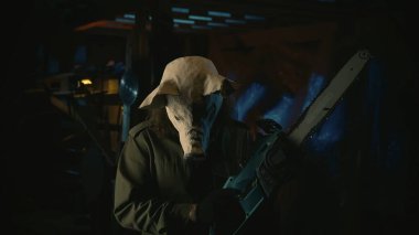 Korku filmi sahnesi. Domuz maskeli bir adam eski deponun içinde elektrikli testere tutuyor. Vintage maskeli bir erkek modelin yakın portresi. Cadılar Bayramı konsepti.