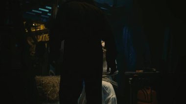 Korku filmi sahnesi. Beyaz elbiseli bir manyağın genç kız kurbanı sandalyeye oturmuş, iple bağlanmış. Bıçak tutan ve önünde duran bir adam..