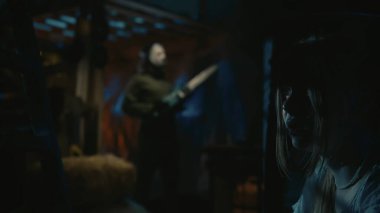 Cadılar Bayramı film sahnesi. Kız model, fıçının arkasında saklanan korku manyağının kurbanı. Elektrikli testereli bir adam etrafta dolaşıyor..
