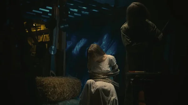 恐怖的电影场景 恐怖狂热者的女性受害者坐在仓库的椅子上 被绳子捆住的女孩 寻找杀人工具的人 — 图库照片