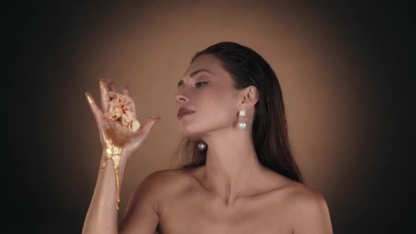 美しいブルネットの女性の肖像画 彼女の手から流れる黄金の絵を見て それに触れる真珠のイヤリングを持つ女性モデルのクローズアップショット ビューティー広告コンセプト — ストック動画