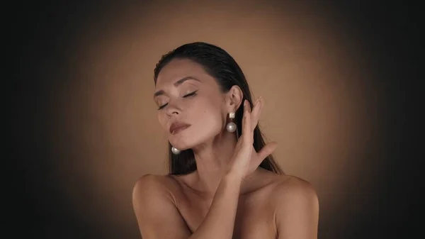 美しいブルネットの女性の肖像画 メイクと真珠のイヤリングで彼女の滑らかな肌に触れる女性モデルのスタジオショットを閉じます ビューティー広告コンセプト — ストック写真
