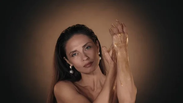 一个美丽的高加索女人的画像 女性模特的特写镜头 在手上的皮肤上涂上金光闪闪的液体颜料 美容广告概念 — 图库照片