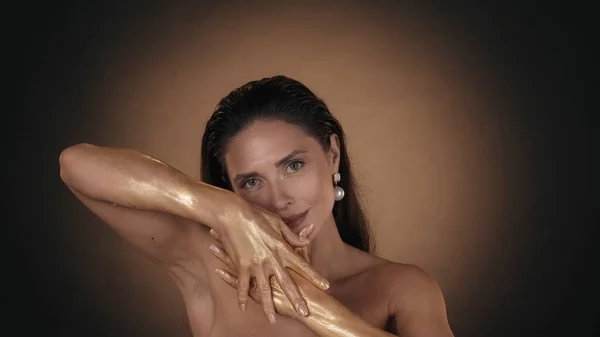 一个漂亮女人的画像 用闪亮的化妆品在手上的皮肤上涂上金色液体涂料的女性模特的近照 看着相机 美容广告概念 — 图库照片