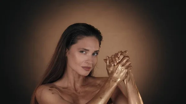 一个迷人女人的画像 用闪亮的化妆品在手上的皮肤上涂上金色液体涂料的女性模特的近照 看着相机 美容广告概念 — 图库照片