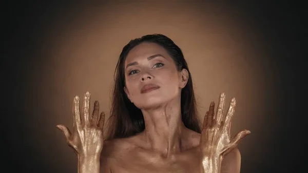 輝く化粧をしたブルネット女性の肖像画 彼女の手に金色の液体塗料を示す女性モデルのクローズアップショット カメラを見ます ビューティー広告コンセプト — ストック写真